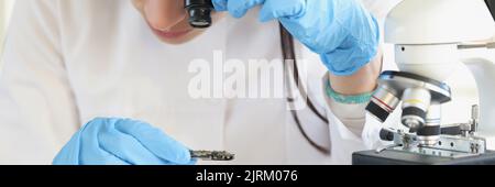 Woman scientist looking through magnifying glass at computer chip near microscope in laboratory Stock Photo