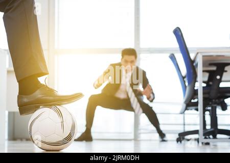 Taking short break from work: two white collar workers having fun together while playing football at spacious open plan office Stock Photo