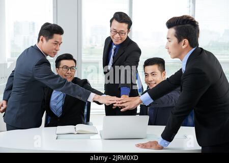 Ambitious team of white collar workers joining hands together while having productive working meeting at modern boardroom Stock Photo