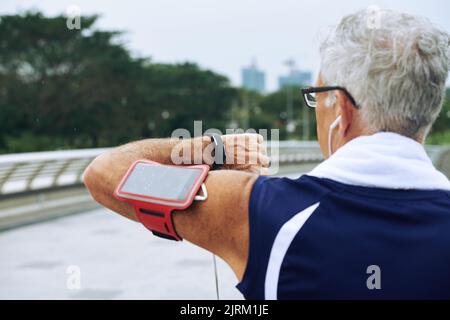 Rear view of elderly runner checking heart rate on fitness tracker when training Stock Photo