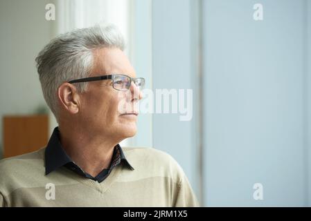 Portrait of pensive senior man looking through window Stock Photo