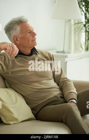 Elderly man sitting on sofa deep in thoughts Stock Photo