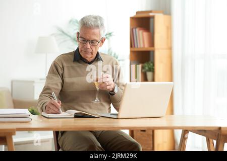 Senior man drinking wine when working at home Stock Photo