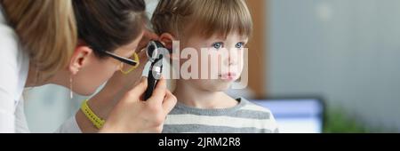 Female pediatrician looking at ear of little girl using otoscope in clinic Stock Photo