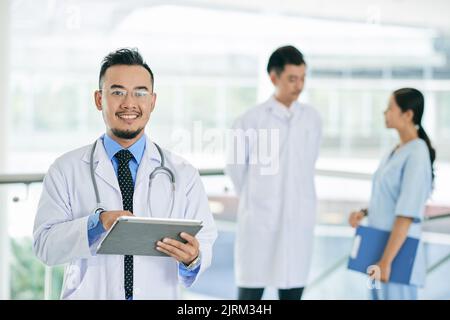 Cheerful mature Vietnamese doctor working on tablet computer Stock Photo