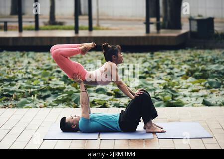 Young Vietnamese couple doing acroyoga asana outdoors Stock Photo