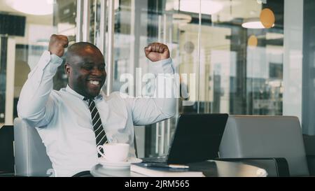 Successful african american businessman using laptop computer receiving good message and become very excited and dancing while sitting in modern cafe duiring coffee braek Stock Photo