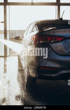 A man washes his car at a self-service car wash using a hose with pressurized water. Stock Photo