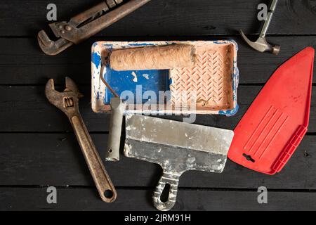 gas wrench hammer roller in paint in a tray and a spatula lie on a black wooden floor, repair tools, repair tool kit Stock Photo