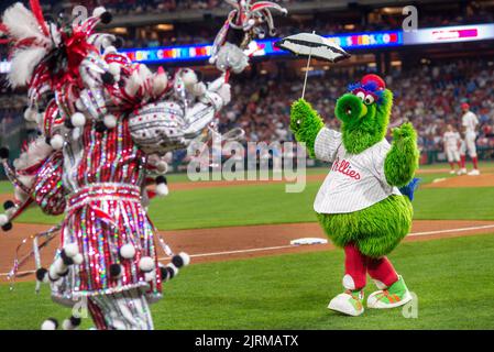 WMMR's Jacky Bam Bam wears his prize winning Mummers costume as he dances on field at third base with the Phillies Phanatic between the 5th and 6th innings of the Cincinnati Reds at Philadelphia Phillies baseball game Wednesday, August 24, 2022 at Citizens Bank Park in Philadelphia, Pennsylvania. The Phillies held Mummers Night in celebration of the group and their New Years Parade tradition. Thirty percent of Phillies ticket sales went to the Mummers clubs, who now fund the annual parade themselves after the city of Philadelphia stopped offering prize money a number of years ago. Stock Photo