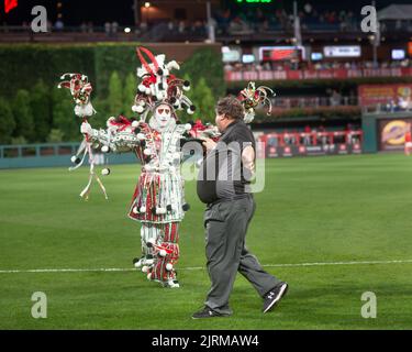 Philadelphia, United States. 24th Aug, 2022. WMMR's Jacky Bam Bam wears his prize winning Mummers costume as he dances on field while teasing faux umpire Chris Morris at third base with the Phillies Phanatic between the 5th and 6th innings of the Cincinnati Reds at Philadelphia Phillies baseball game Wednesday, August 24, 2022 at Citizens Bank Park in Philadelphia, Pennsylvania. The Phillies held Mummers Night in celebration of the group and their New Years Parade tradition. Credit: William Thomas Cain/Alamy Live News Stock Photo