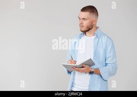 handsome man in blue shirt writing note in notebook Stock Photo