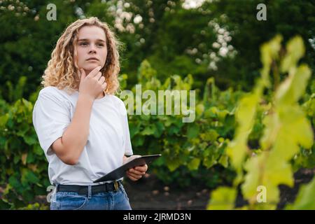 Free space for text. Woman with curly hair wearing a t-shirt, being bothered by the negative data recorded in the tablet she is holding. Thoughtful Stock Photo