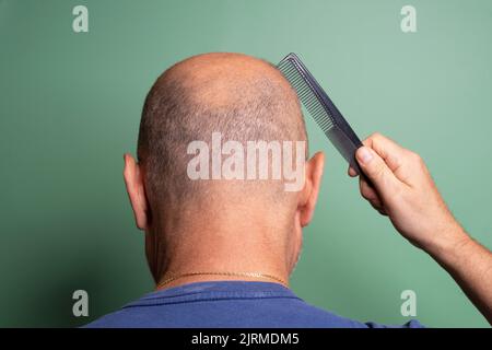 view from behind of a bald man while he combs his hair Stock Photo