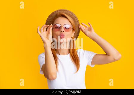 Young redhead woman in straw hat, surprised expression, isolated on yellow background. Summer lifestyle studio portrait. Redhead girl sends an air Stock Photo