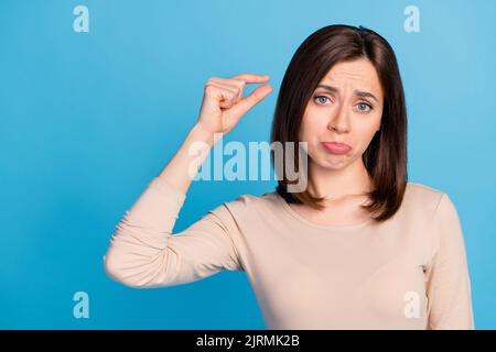 Portrait of unsatisfied person sullen face arms fingers demonstrate little size isolated on blue color background Stock Photo