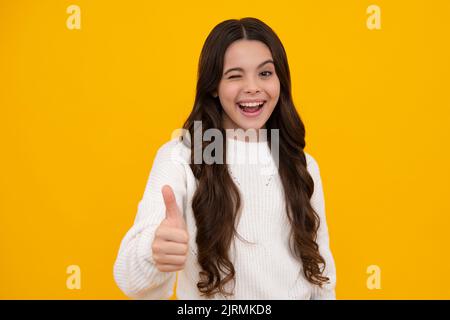 Like it. Portrait of joyful teenage child girl showing thumbs up and smiling, yellow background with copy space. Excited teenager girl. Stock Photo