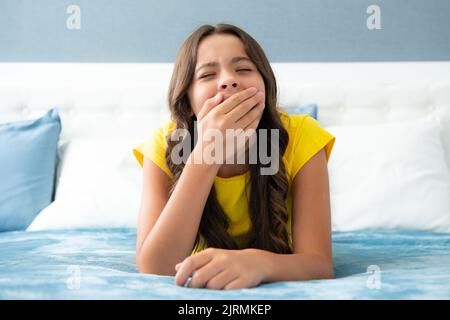 Tired lazy teenager girl yawning in bed. Sleepless child wake up on bed and yawning feeling tired. Stock Photo