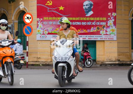 Vietnamese girls on motorcycles in front of Ho Chi Minh propaganda poster, Hai Phong, Vietnam Stock Photo