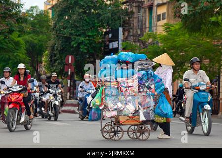 Vietnamese street trader with pushcart among motorcycles at traffic junction, Hai Phong, Vietnam Stock Photo