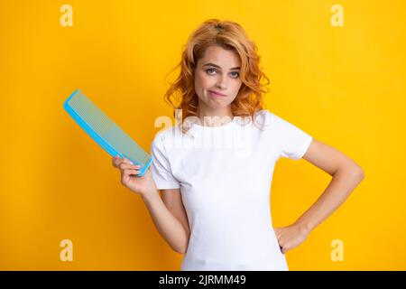 Surprised amazed girl combing hair. Redhead woman with a comb, isolated on yellow background. Woman is upset of hair loss. Portrait of sad girl with Stock Photo