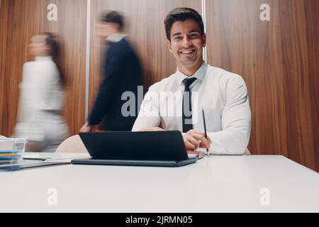 Businessman using laptop sit at table in office meeting background with walking people with motion blur. Business people man and woman group conference discussion. Stock Photo