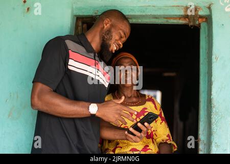 african man explaining to an elderly african woman with phone Stock Photo