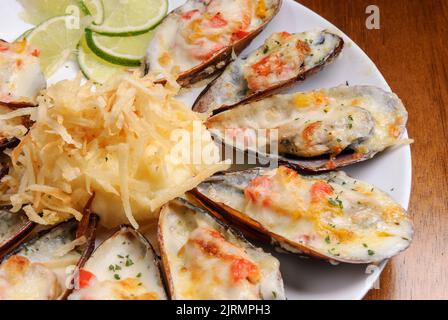 Baked mussels au gratin with mashed potatoes on a white plate on wooden table. Brazilian seafood. Stock Photo