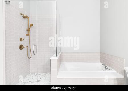 A bathroom with a renovated shower and bathtub. The shower features a gold faucet, subway tile walls, and a hexagon tiled floor. Stock Photo