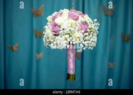 Bridals bouquet with purple roses, levitating on blue fabric folds background with defocused golden butterflies Stock Photo