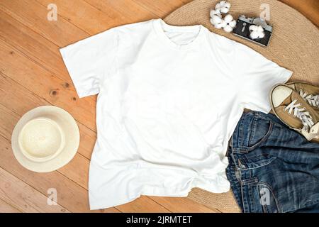 Unisex white shirt , flat lay on wooden boards with blue jeans, sneakers and cotton flowers, Creative mockup for design presentation. Stock Photo