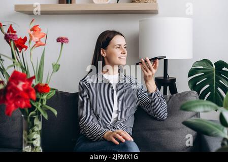 Attractive young woman listening pleasant news in audio message, recording response using cellphone application. Happy female communicating distantly Stock Photo