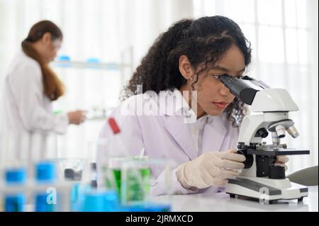 Young scientist looking in microscope while working on medical research in science laboratory Stock Photo