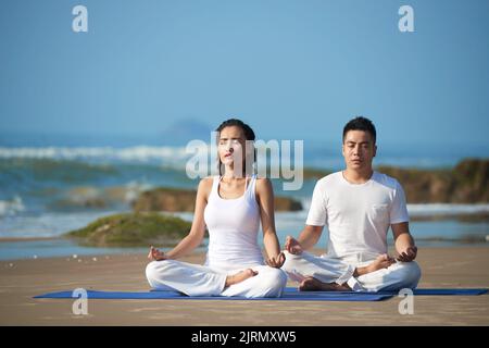 Young Vietnamese couple meditating on the beach Stock Photo