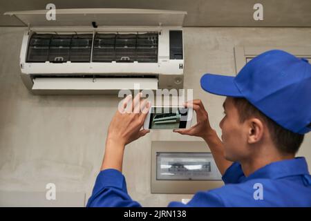 Technician photographing installed air conditioner on smartphone Stock Photo