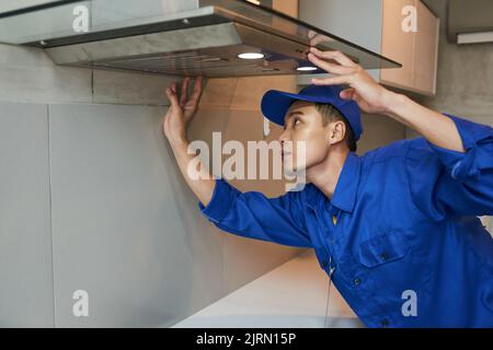 Young Vietnamese technician installing extractor hood in kitchen Stock Photo