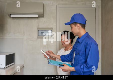 Technician explaining senior Vietnamese woman how to use air conditioner Stock Photo