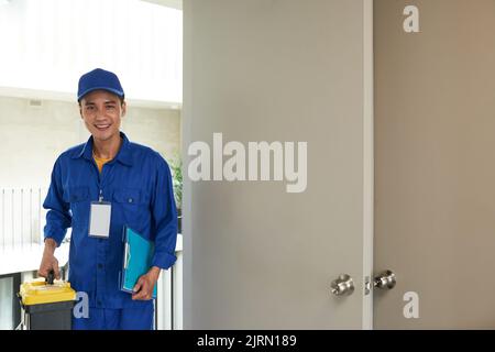 Smiling young handyman with toolbox entering home Stock Photo