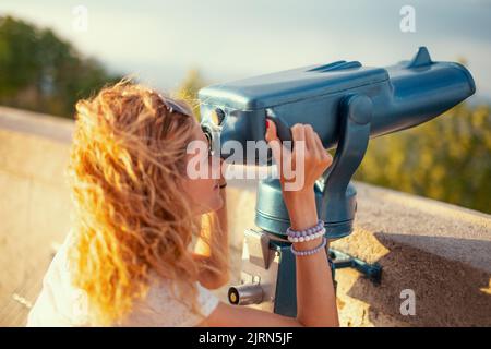 Readhead 30s woman looking through telescope while sightseeing at autumn Stock Photo