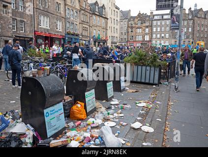 City centre Edinburgh, Scotland, UK. 25th August 2022. Cloudy but mild 19 degrees centigrade for the FC Zurich fans who gathered surrounded by Police Officers in the untidy Grassmarket to peacefully socialise before this evening's game with Heart of Midlothian. Also, smaller crowds in the Royal Mile for street performers. Pictured: Rubbish still piled up at refuse bins due to strike with FC Zurich fans in background having a drink in the Grassmarket. Credit: ArchWhite/alamy live news. Stock Photo