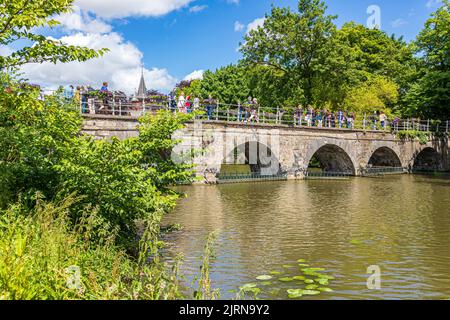 Tourists crossing the Minnewaterbrug (Lovers Bridge) over the Minnewater (Lake of love) in Bruges, Belgium Stock Photo