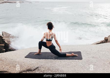 Young woman practicing yoga on mat by ocean at evening Stock Photo