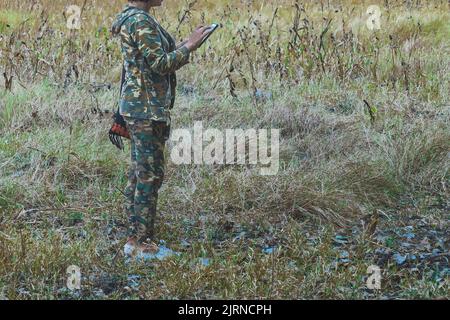 Female forest ranger in uniform uses cell phone to monitor the fertility of the land in the national park conservation area. Woman using mobile phone Stock Photo