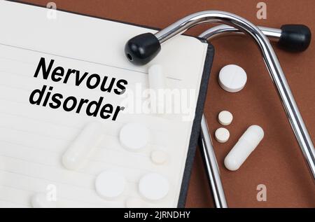 Medical concept. On a brown surface lies a stethoscope, pills and a notepad with the inscription - Nervous Disorder Stock Photo