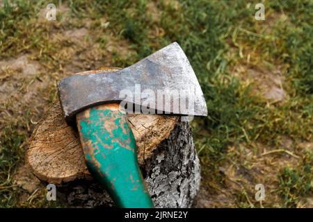 Defocus steel ax closeup. Big steel axe with wooden handle, metal ax for wood chopping. Green nature background. Forged axe it main accessory male, na Stock Photo