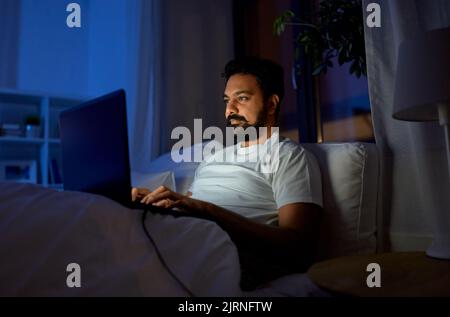 indian man with laptop in bed at home at night Stock Photo