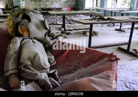 Gas mask on a doll's head in Prypiat classroom. Chernobyl Exclusion Zone Stock Photo