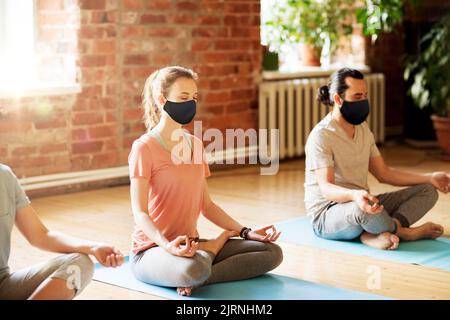 group of people in masks meditating at yoga studio Stock Photo