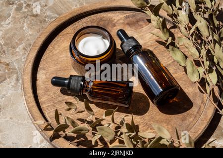 Amber glass containers with natural cosmetics and eucalyptus on wooden tray on table in bathroom. SPA organic bio cosmetics set Stock Photo