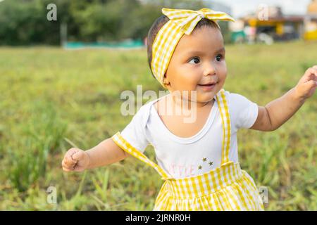 little latin girl standing in a grassy field, smiling and looking very happy. beautiful summer day in the colombian coffee region. brown skinned baby Stock Photo